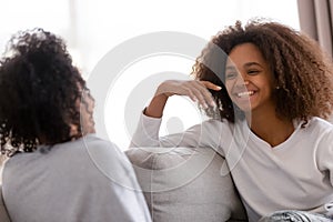 Happy african mother and daughter talking laughing sitting on sofa