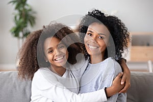 Happy african mother and teen daughter embracing looking at camera