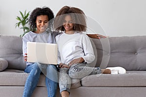 Happy african mother and teen daughter using laptop on sofa