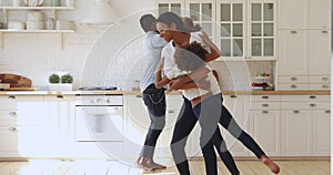 Happy african parents holding kids having fun dancing in kitchen