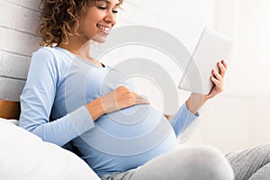 Happy african pregnant woman reading E-Book on tablet