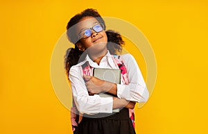 Happy African Schoolgirl Embracing Book Over Yellow Studio Background