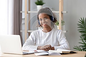 Happy african schoolgirl wearing headphones e-learning using computer