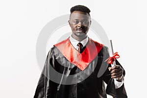 Happy african student in black graduation gown and cap raises masters degree diploma above head on white background