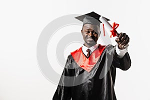 Happy african student in black graduation gown and cap raises masters degree diploma above head on white background