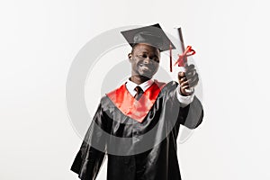 Happy african student in black graduation gown and cap raises masters degree diploma above head on white background