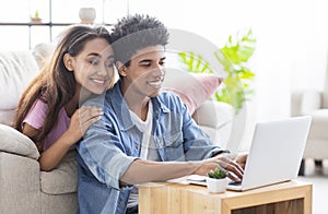 Happy african teen couple working together on laptop at home.