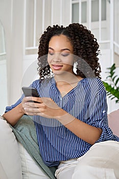 Happy African teen girl holding cell phone using smartphone at home.