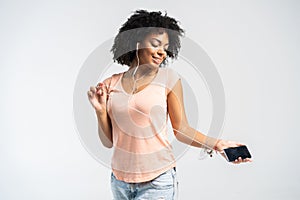 Happy african woman with afro and casual clothing dancing to the music she is listening to from her phone.