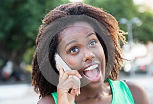 Happy african woman in a green shirt outdoor at phone