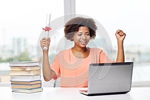 Happy african woman with laptop, books and diploma