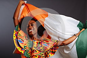 Happy african woman in national clothes smiling and posing with a flag Ivory Coast, C te d`Ivoire isolated over a gray