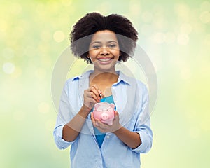 Happy african woman putting coin into piggy bank