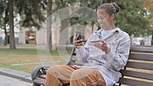 Happy African Woman Shopping Online on Smartphone, Sitting Outdoor on Bench