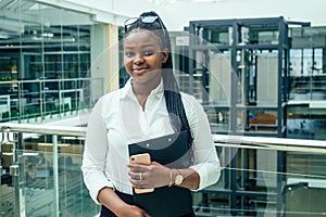 Happy African woman in a stylish skirt and shirt in a modern office with panoramic windows shopping center