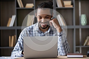 Happy African worker in casual working at laptop