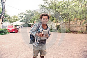 Happy african young man holding backpack and books