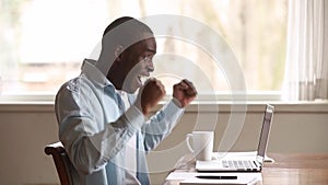 Happy african young man reading great news online using laptop