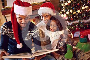 Happy afro American family read a book at fireplace on Christmas