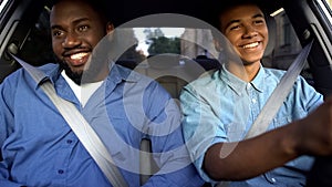 Happy afro-american father and teen sitting in car, dad pleased with sons drive