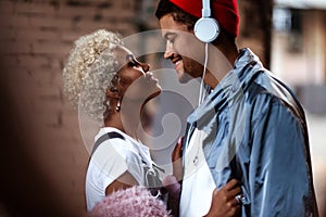 Happy Afro American man in heaphones and his dark skinned female with curly hairdo stand close to each other, look