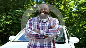 Happy afro-american man smiling on cam, leaning new automobile, rent service