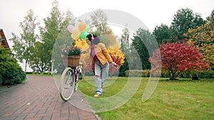 Happy Afro-American woman dancing near ladies bike in a park with autumn trees