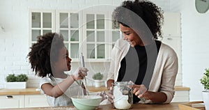 Happy afro-american young mum and cute child daughter whisking dough