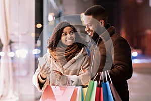 Happy afro couple using smartphone with shopping bags