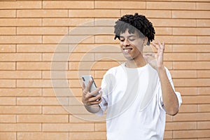 A happy Afro man holding a phone and showing an OK sign to the camera during an online meeting