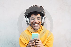 Happy Afro man using mobile smartphone outdoor - Young guy having fun listening music with wireless headphones outdoor