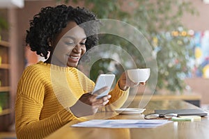 Happy afro woman drinking coffee and using mobile phone