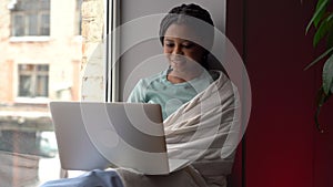 Happy afro woman use laptop at home. Joyful female sit at windowsill messaging with friend on pc