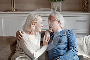 Happy aged couple cuddle on couch having talk