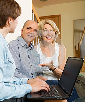 Happy aged couple talking with employee with laptop