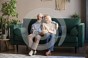 Happy aged couple, wife and husband watching tv and eating popcorn