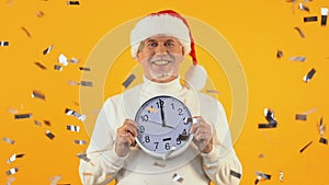 Happy aged man in santa hat holding clock showing midnight, New Year party