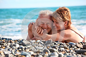 Happy aged pair lie on pebble beach