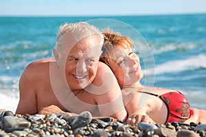 Happy aged pair lie on pebble beach