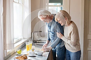 Happy aged woman embrace husband cooking healthy breakfast