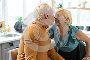 Happy alluring aging spouse tenderly kissing her aged grey-haired husband.