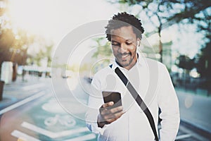 Happy american African man using smartphone outdoor.Portrait of young black cheerful man texting a sms message while