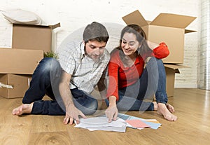 happy American couple sitting on floor moving in new house looking blueprints