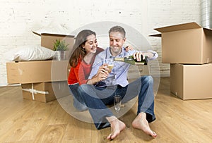 Happy American couple sitting on floor unpacking together celebrating with champagne toast moving in a new house