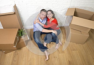 Happy American couple sitting on floor unpacking together celebrating moving to new house flat or apartment
