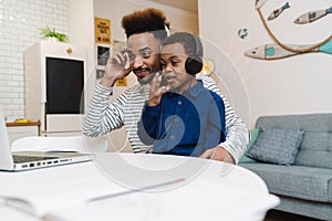 Happy american father and son in headphones using laptop at home