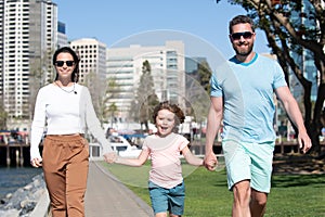 Happy american parents holding hands with son and walking in sunny summer citi street, tender family moment. Family