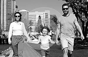 Happy american parents holding hands with son and walking in sunny summer citi street, tender family moment. Family