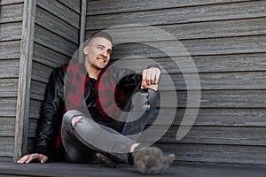 Happy American stylish young man in a fashionable checkered jacket with leather sleeves in ripped stylish jeans in sneakers