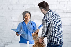 Happy animal doctor talking to male client with cute little doggy at veterinary clinic